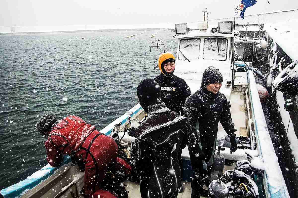 Group of divers kitted up on a boat in snowy conditions near hokkaido 