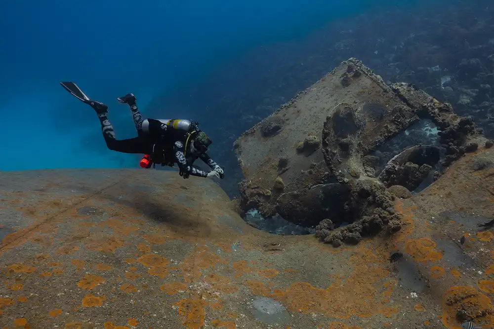 A diver swims next to Hilma Hooker’s propellers and rudder with the backdrop of the surrounding reef.