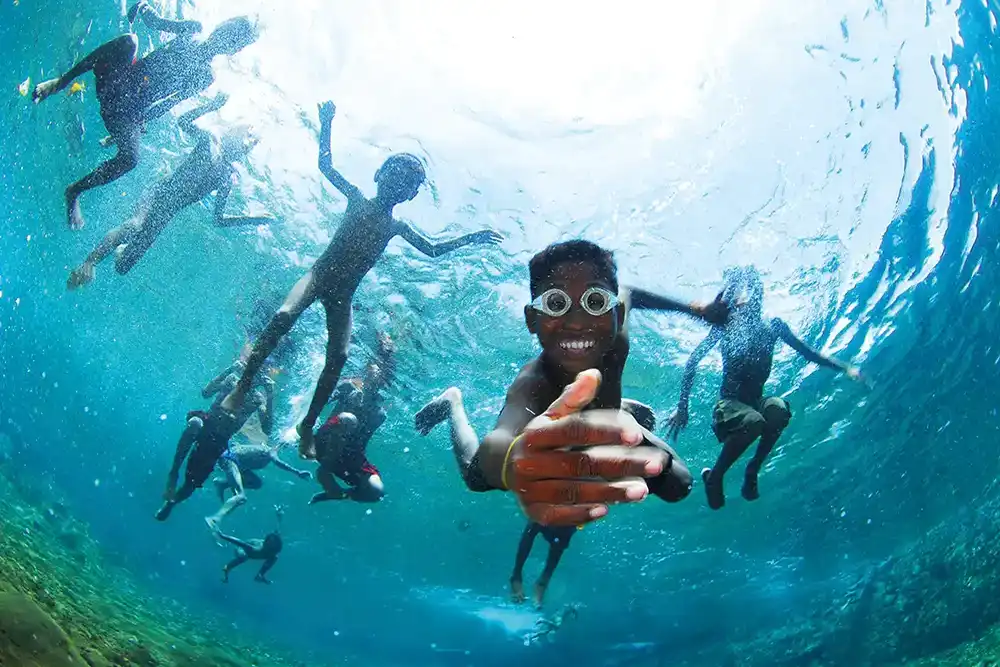 children swimming over the reef while a diver takes a photograph from below