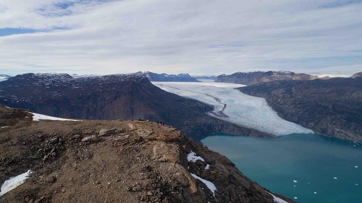 hikers on a mountaintop with a glacier in the background in the fjords of scoresby sund