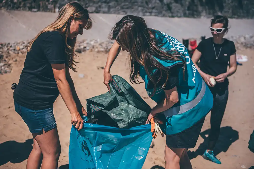 Three women putting beach litter into a large rubbish bag during a beach cleaning event