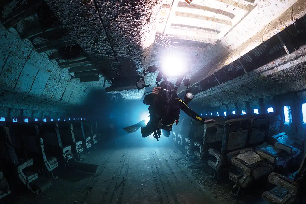 a diver with a camera swimming inside the wreck of a sunken lockheed tristar
