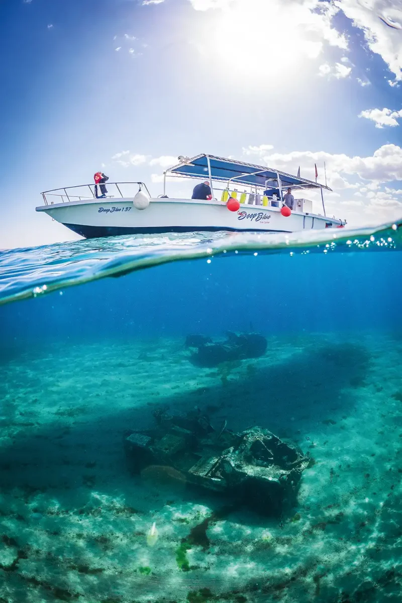 a split shot of a boat sailing over two sunken jeeps in Aqaba