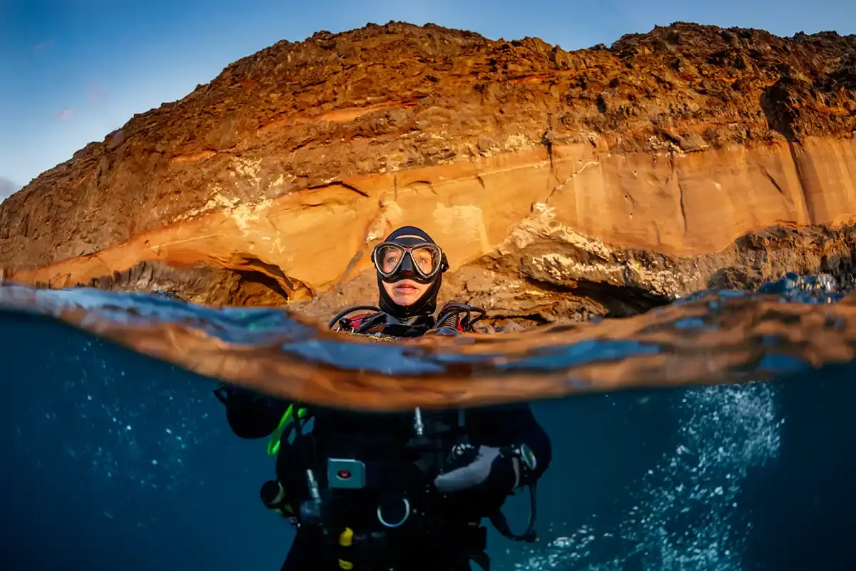 A diver surfacing in the clear blue waters alongside St Helena's beautifully rugged coastline