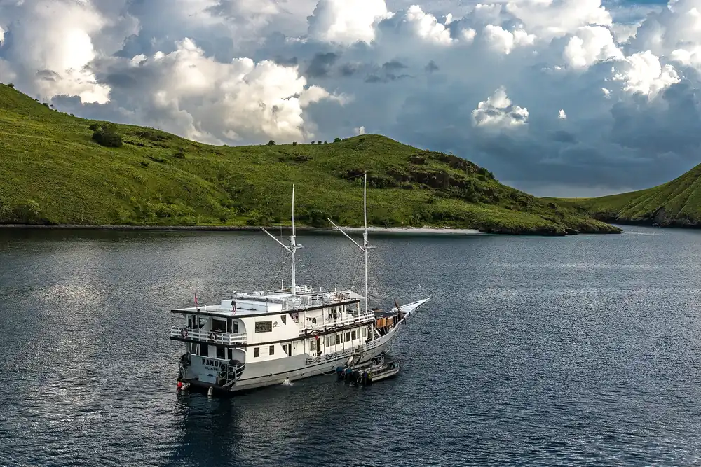 Komodo Aggressor moored in a bay beneath green island hills
