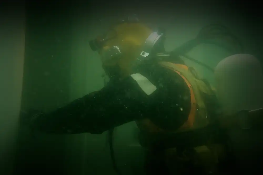 a commercial diver in a diving helmet enters the door of an upturned boat wreck