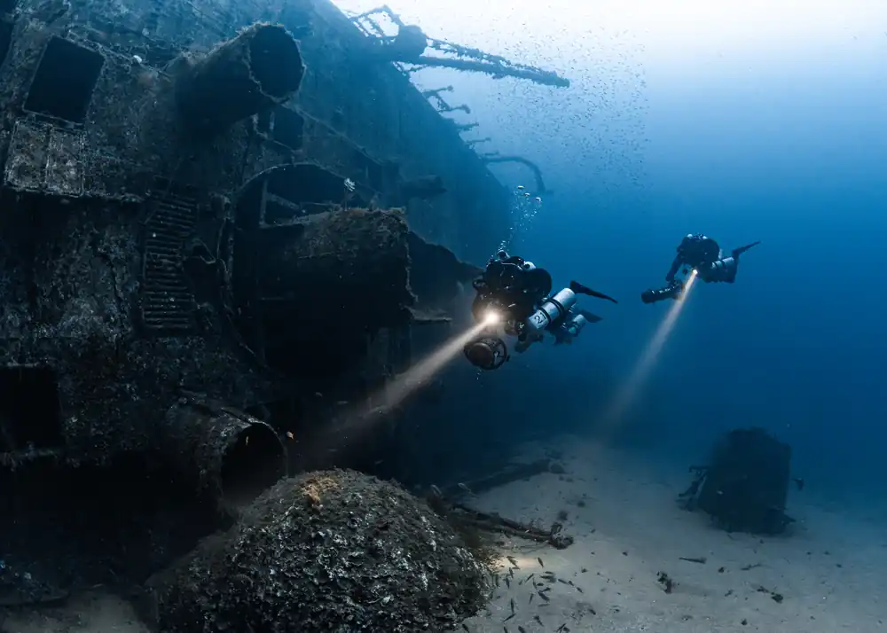 Divers exploring the Isonzo wreck with torch beams
