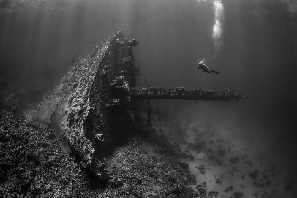 Black-and-white view of the Giannis D wreck with a diver and trail of bubbles