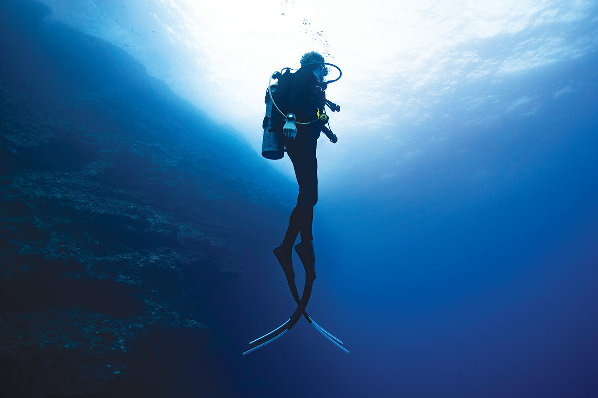 Scuba diver in blue ocean diving next to wall