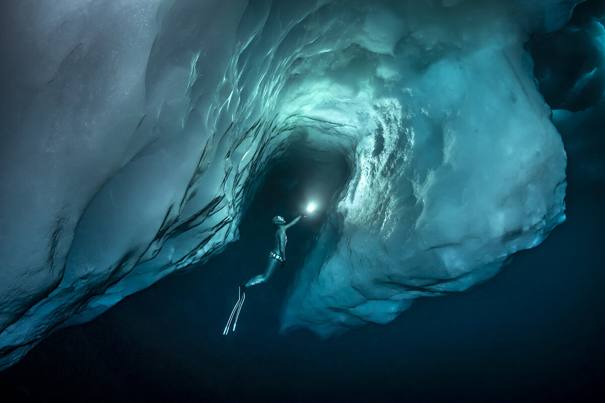 A diver illuminates under the ice with a torch