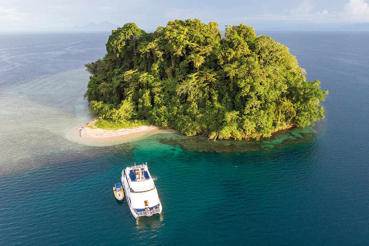 A white boat moors up at the greet forested Restorf Island