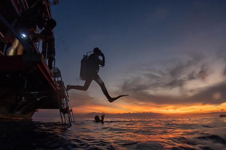 divers jumping off a boat at sunset