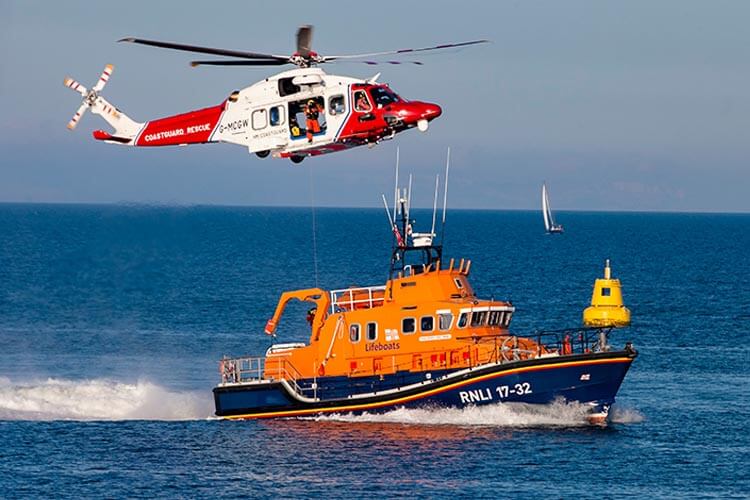 picture of a RNLI lifeboat at sea and a Coastguard helicopter hovering above it